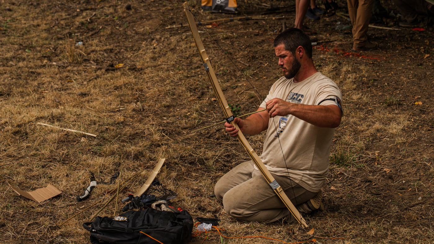 A competitor kneeling in a field to string a wooden bow during the 2026 Survival Games