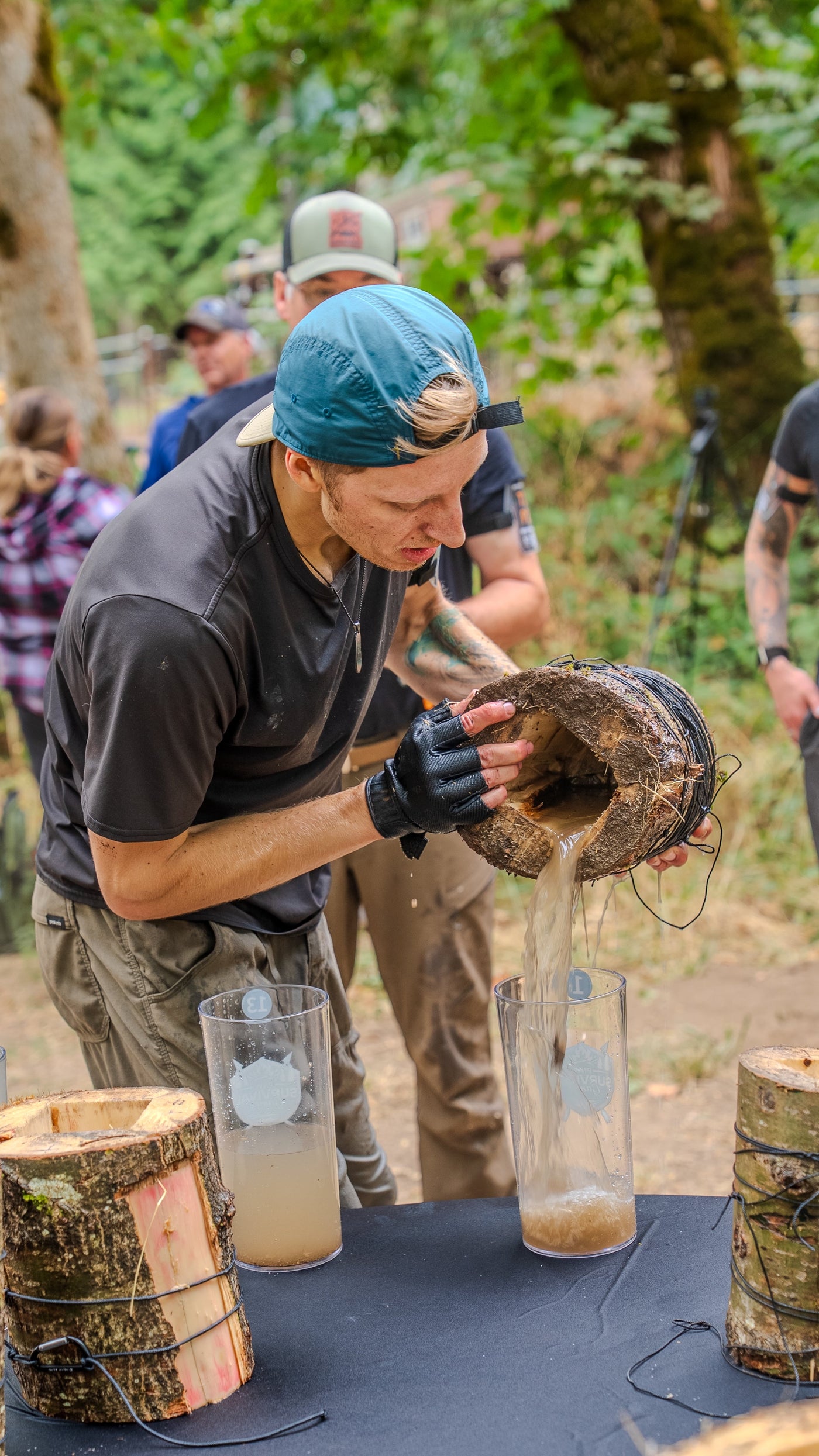 A competitor pouring water from a hollowed log into a cup during the 2026 Survival Games
